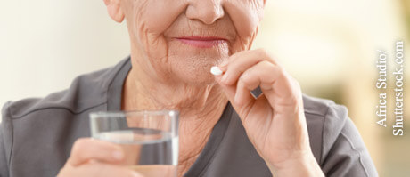 Frau hält ein Glas mit Wasser und eine Tablette in den Händen. Augentropfen können mit oral eingenommenen Arzneien wechselwirken.
